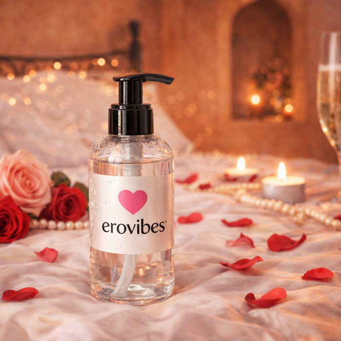 Lubricante Erovibes sobre una cama romántica con pétalos de rosa, velas y una copa de cava.